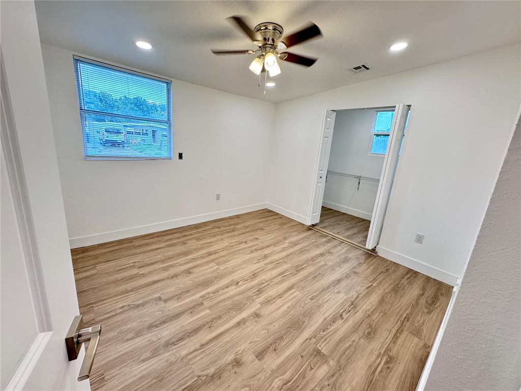 A bedroom features light wood-look flooring, white walls, a ceiling fan, and an open closet — 7913 TIDEWATER TRAIL, TAMPA, FL