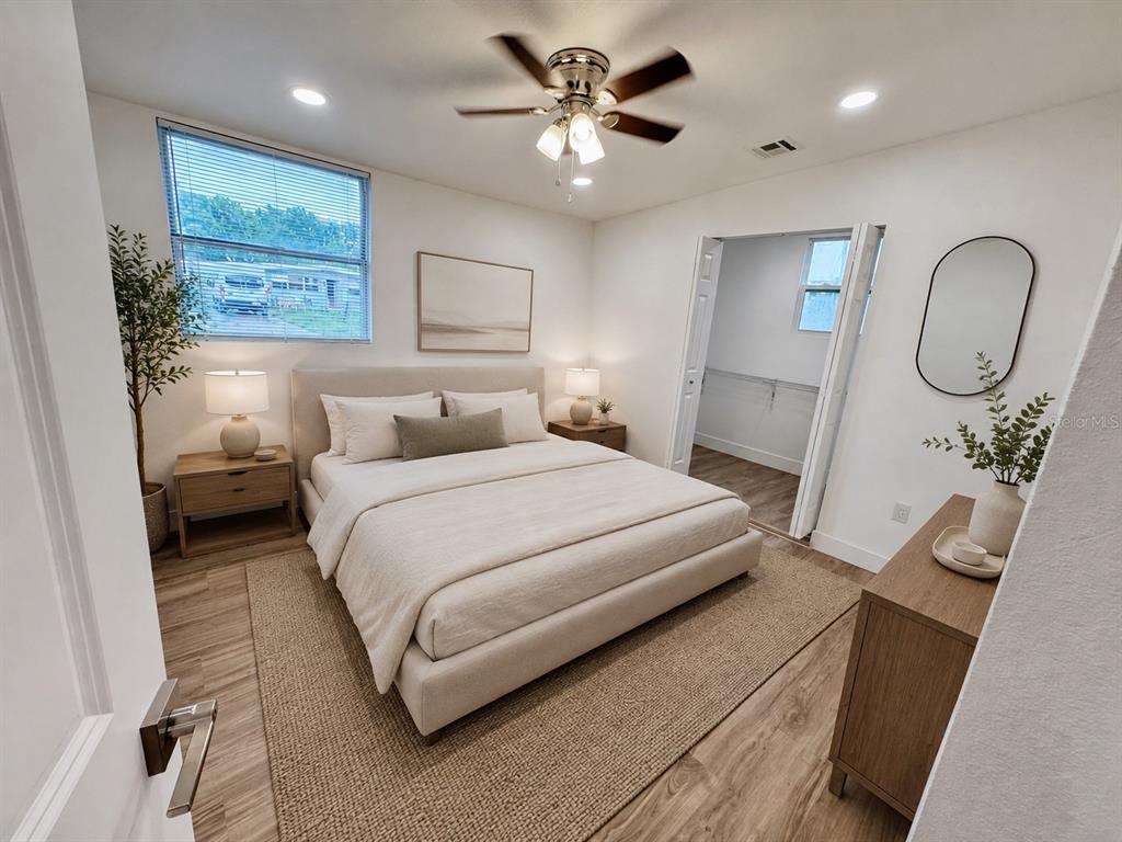 A modern bedroom features a neutral upholstered bed, wood-look flooring, a ceiling fan, and walk-in closet — 7913 TIDEWATER TRAIL, TAMPA, FL