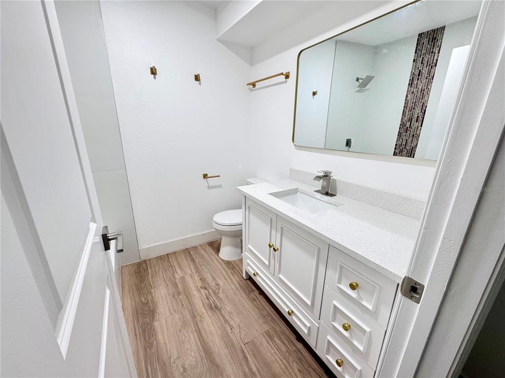 A bathroom features a white vanity with a quartz countertop, a mirror, and wood-look flooring — 7913 TIDEWATER TRAIL, TAMPA, FL