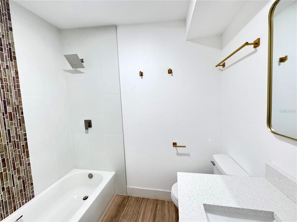 A bathroom features a white bathtub, a vanity with a stone countertop, and gold fixtures — 7913 TIDEWATER TRAIL, TAMPA, FL