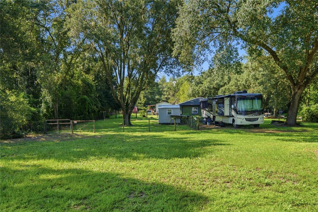 A large recreational vehicle is parked on a grassy lot near a small house and shed — 19791 SE 110TH COURT, INGLIS, FL