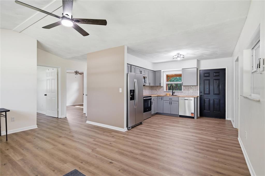 A kitchen with gray cabinets, stainless steel appliances, and wood-look flooring opens to a living area — 19791 SE 110TH COURT, INGLIS, FL