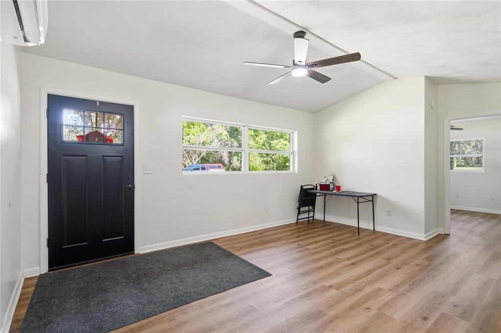 A living room with light walls, wood-look flooring, a ceiling fan, and a black front door — 19791 SE 110TH COURT, INGLIS, FL