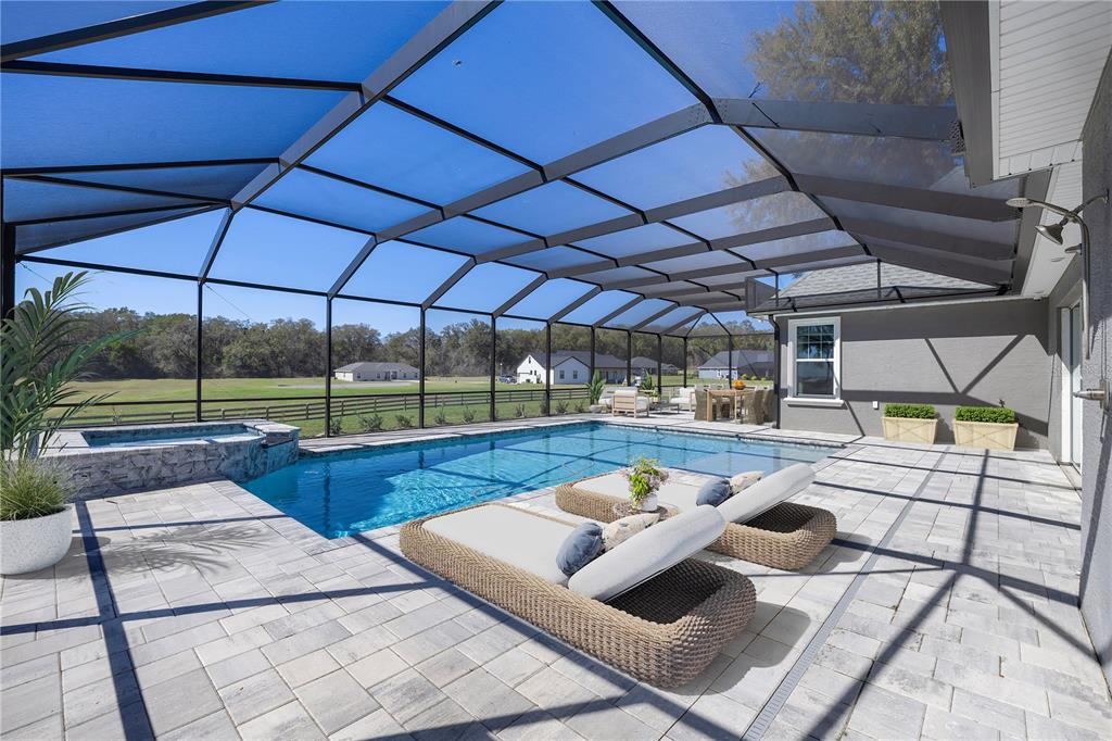 A screened-in patio features a swimming pool, a hot tub, and lounge chairs on pavers — 1873 NW 85TH LOOP, OCALA, FL
