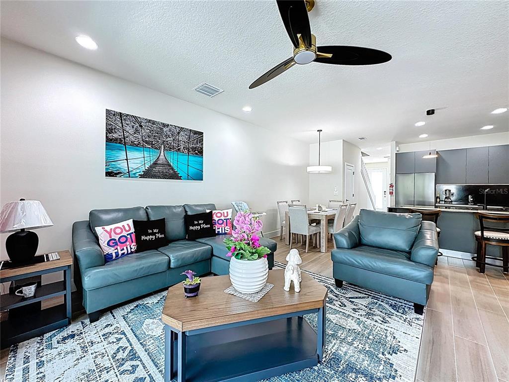A living room with a blue sectional, matching armchair, coffee table, and open kitchen area — 1425 SERENDIPITY LANE, CLERMONT, FL