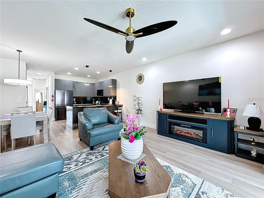 An open-concept living room features a blue media console with a fireplace and a ceiling fan — 1425 SERENDIPITY LANE, CLERMONT, FL