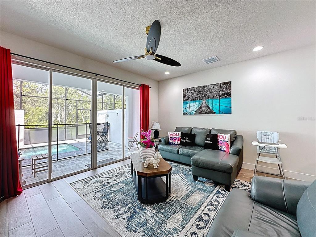 A living room features a grey sectional sofa, a patterned rug, and sliding doors to a pool — 1425 SERENDIPITY LANE, CLERMONT, FL