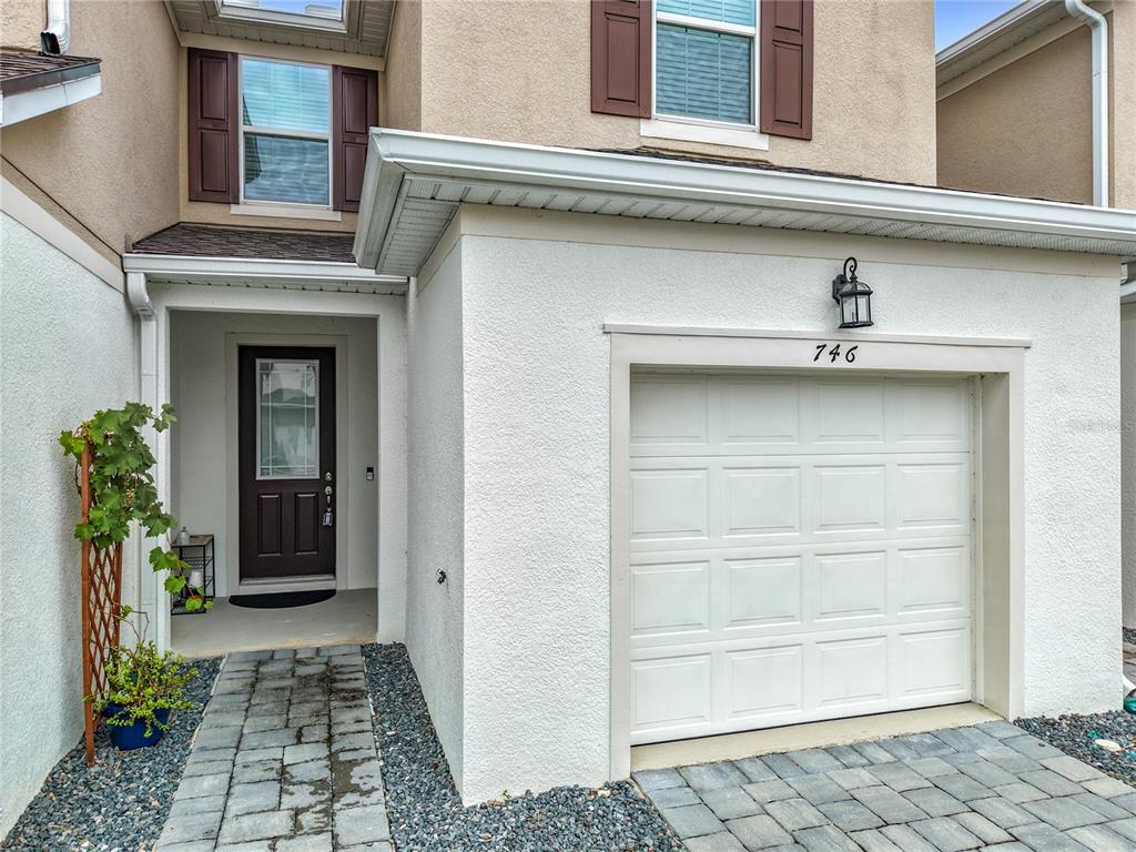 The exterior of a two-story townhouse features a white garage, a front door, and pavers — 746 SPRING PALMS LOOP, ORLANDO, FL