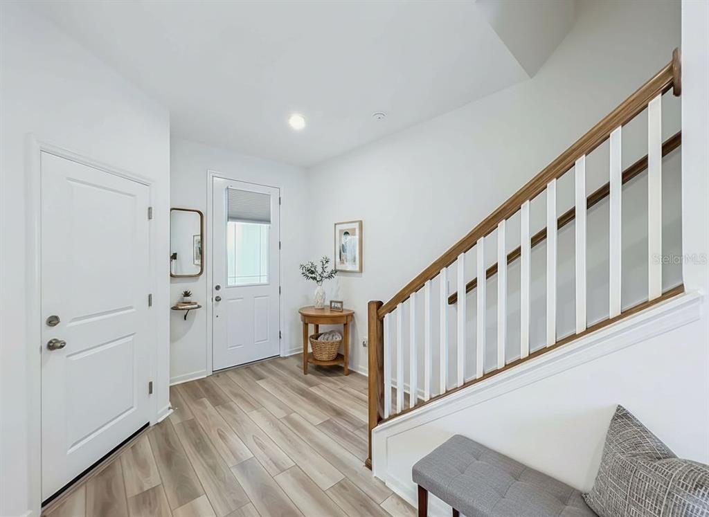 An entryway features light wood-look flooring, a staircase with white railings, and a front door — 746 SPRING PALMS LOOP, ORLANDO, FL