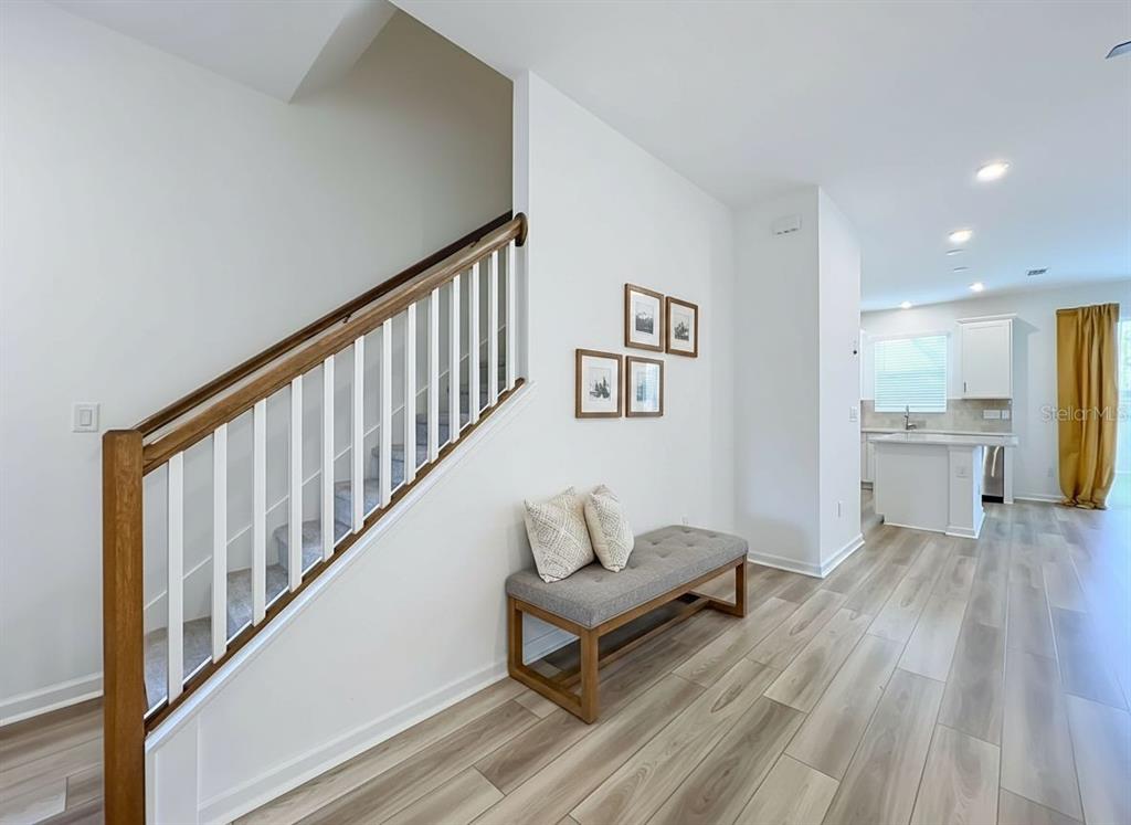 A staircase with a wooden railing sits beside a bench in a modern home interior — 746 SPRING PALMS LOOP, ORLANDO, FL