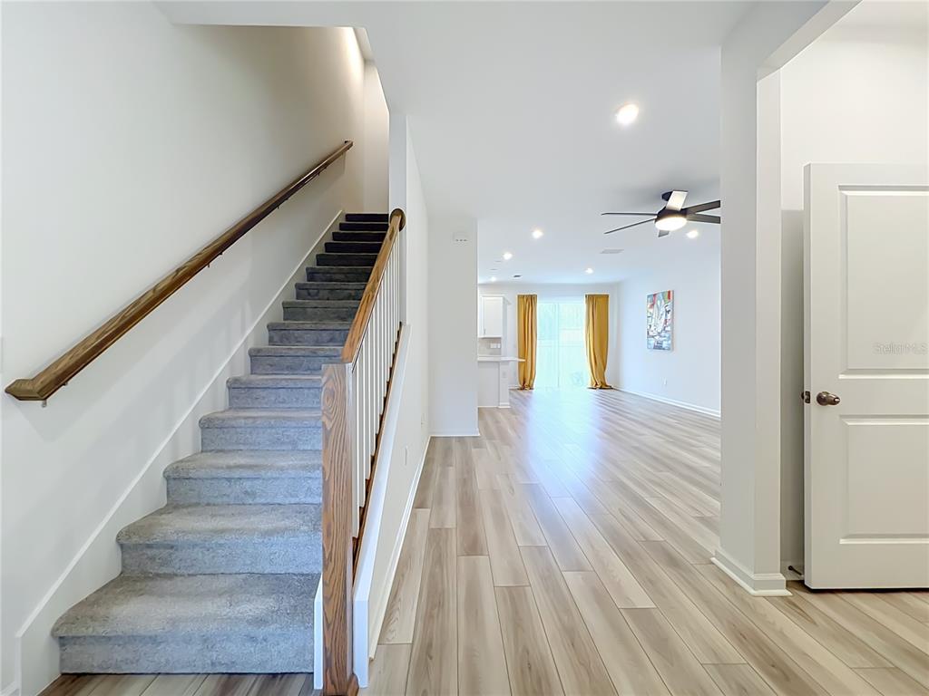 A staircase with gray carpet leads upward next to an open-concept living area with flooring — 746 SPRING PALMS LOOP, ORLANDO, FL