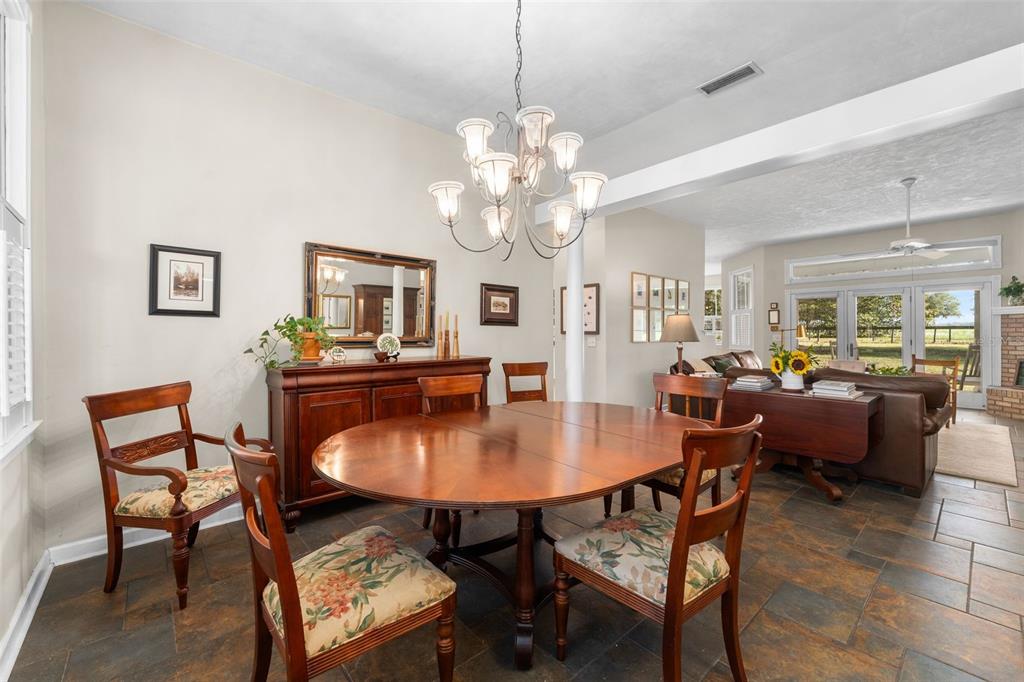 A dining room with a round wooden table, chandelier, and tile flooring opens to a living area — 12934 NW 173RD LANE, ALACHUA, FL