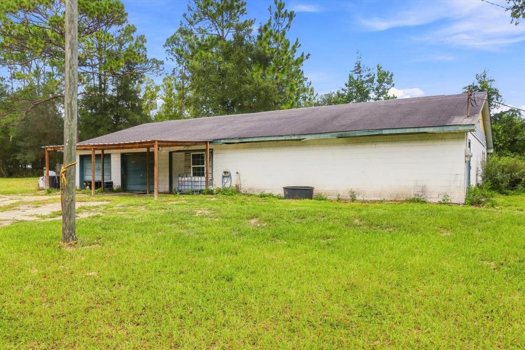 A long, white, single-story concrete block building with a metal-roofed porch and garage doors — 3750 SW 181ST COURT, DUNNELLON, FL