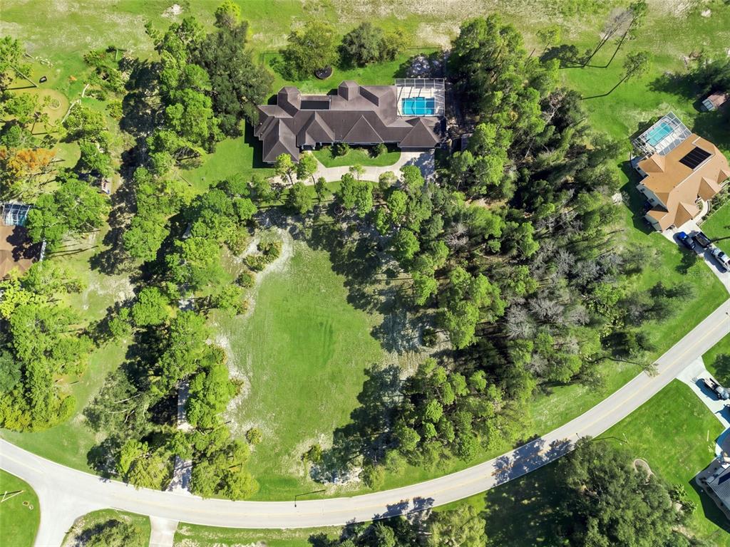 An aerial view shows a large house with a pool surrounded by trees and lawns — 11200 WOODLAND WATERS BOULEVARD, WEEKI WACHEE, FL