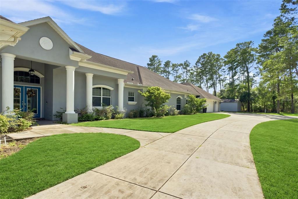 A gray house with white columns and a concrete driveway sits on a grassy lot — 11200 WOODLAND WATERS BOULEVARD, WEEKI WACHEE, FL