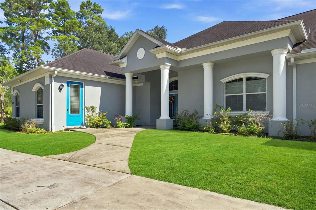 A gray single-story house features white columns, a bright blue door, and a concrete walkway — 11200 WOODLAND WATERS BOULEVARD, WEEKI WACHEE, FL