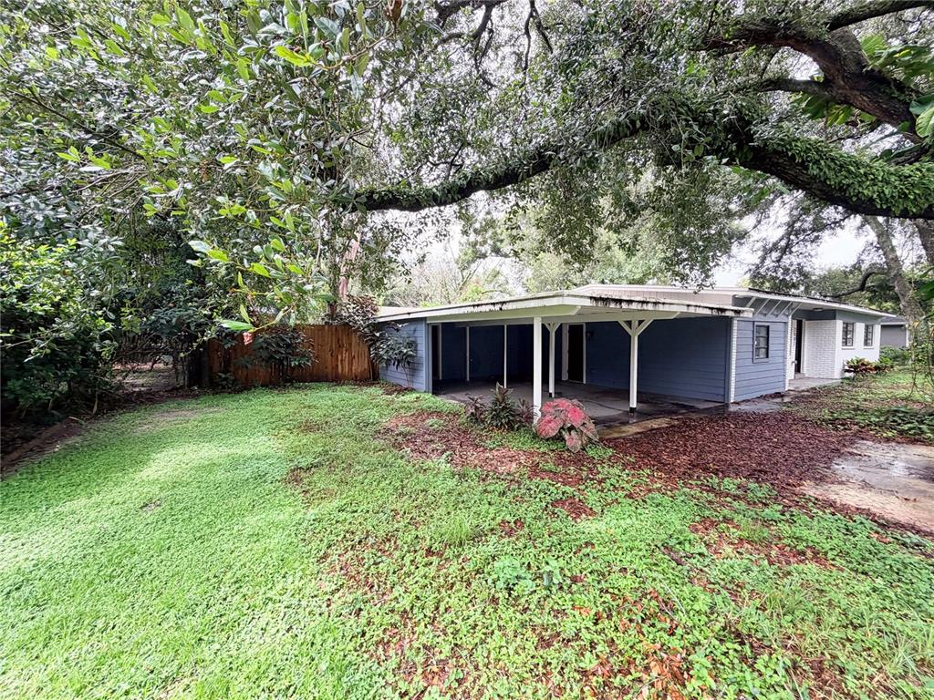 A blue house with a covered patio sits under a large tree in a yard — 2003 E CLINTON STREET, TAMPA, FL