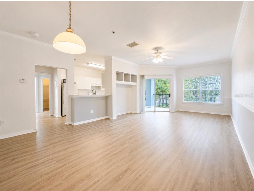 An open-concept living area features light wood-look flooring, a kitchen breakfast bar, and balcony access — 3589 CONROY ROAD UNIT 1023, ORLANDO, FL