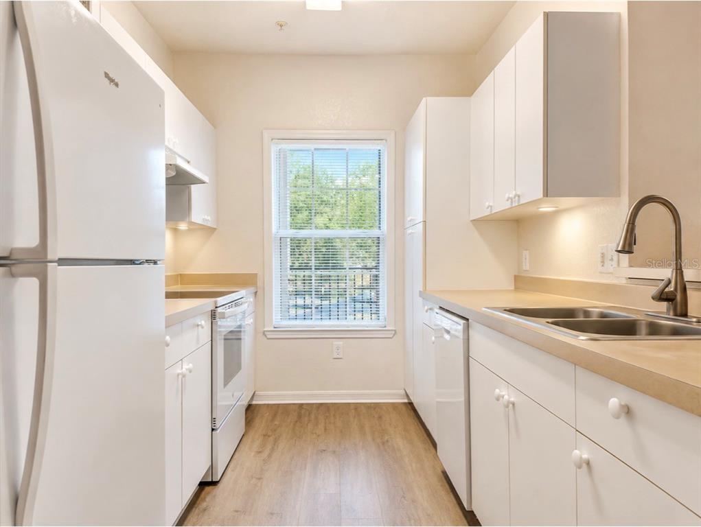 An open-concept living and dining area with light wood floors, neutral furniture, and a kitchen — 3589 CONROY ROAD UNIT 1023, ORLANDO, FL