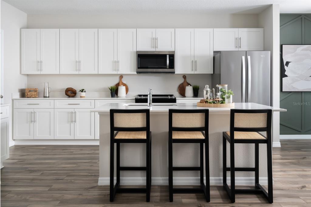 A modern kitchen features white cabinets, stainless steel appliances, a center island, and bar stools — 5386 SAN PIETRO DRIVE, WINTER HAVEN, FL