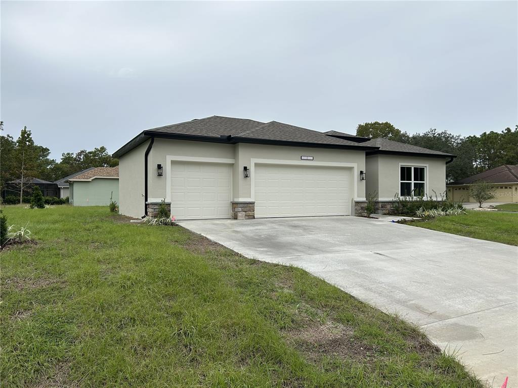 A single-story house with a three-car garage, stone accents, and a concrete driveway — 5887 N BEDSTROW BOULEVARD, DUNNELLON, FL
