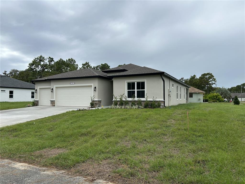 A single-story house with a three-car garage, light stucco exterior, and a dark shingled roof — 5887 N BEDSTROW BOULEVARD, DUNNELLON, FL