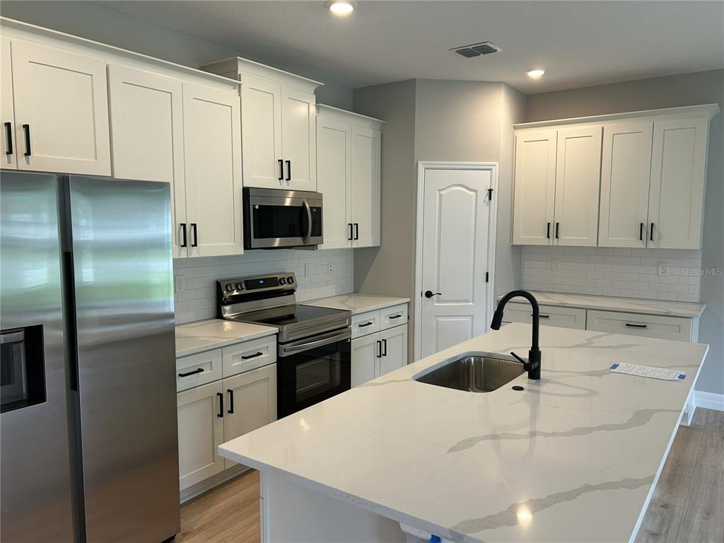 A modern kitchen features white cabinets, stainless steel appliances, and a large quartz-topped island — 5887 N BEDSTROW BOULEVARD, DUNNELLON, FL