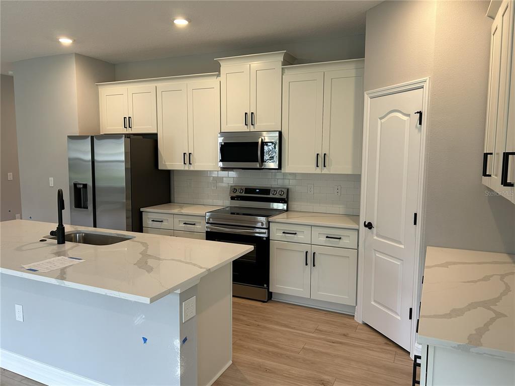 A modern kitchen features white cabinets, stainless steel appliances, and a quartz-topped island — 5887 N BEDSTROW BOULEVARD, DUNNELLON, FL