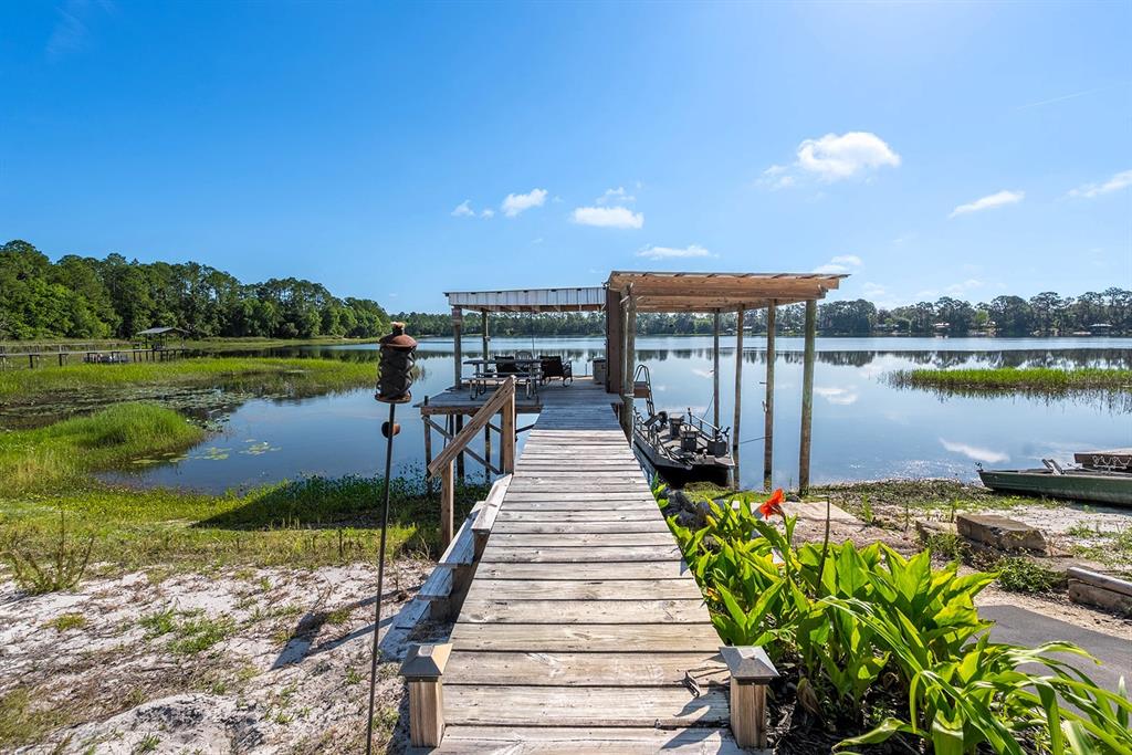 A wooden dock with a covered seating area extends into a calm lake — 588 S COUNTY ROAD 21, HAWTHORNE, FL