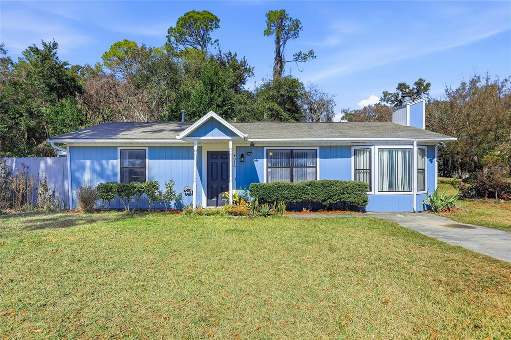 A single-story blue house with a front porch, bay window, and a grassy lawn — 4916 SW 57TH DRIVE, GAINESVILLE, FL