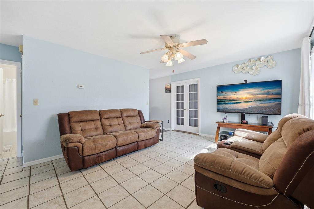 A living room features light blue walls, tile flooring, a ceiling fan, and brown furniture — 4916 SW 57TH DRIVE, GAINESVILLE, FL