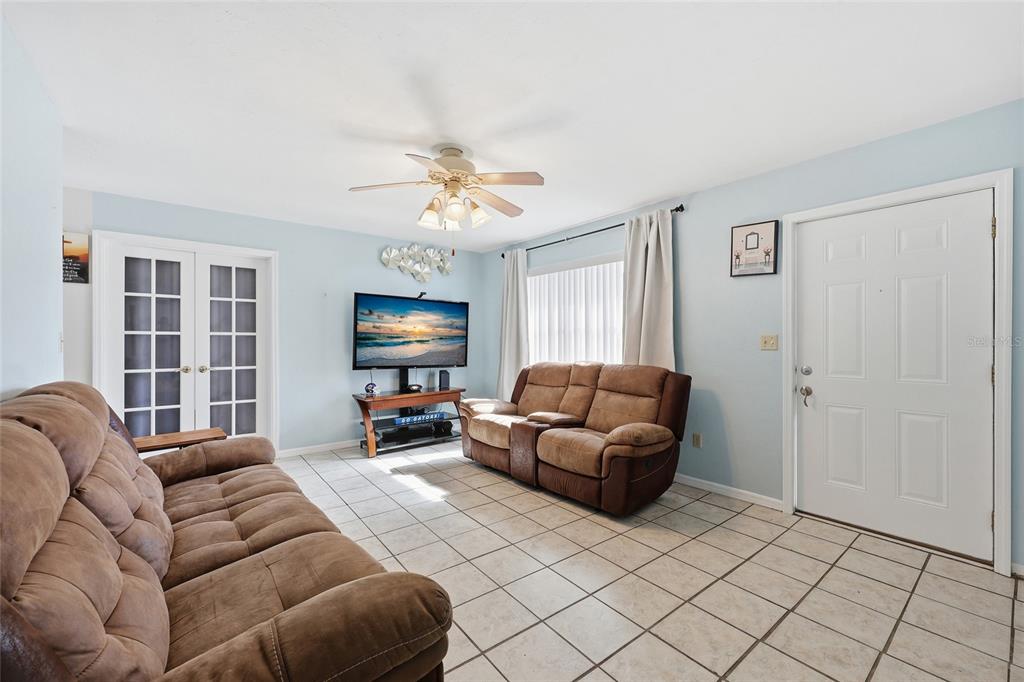 A living room features light blue walls, tile flooring, two brown sofas, and a television — 4916 SW 57TH DRIVE, GAINESVILLE, FL
