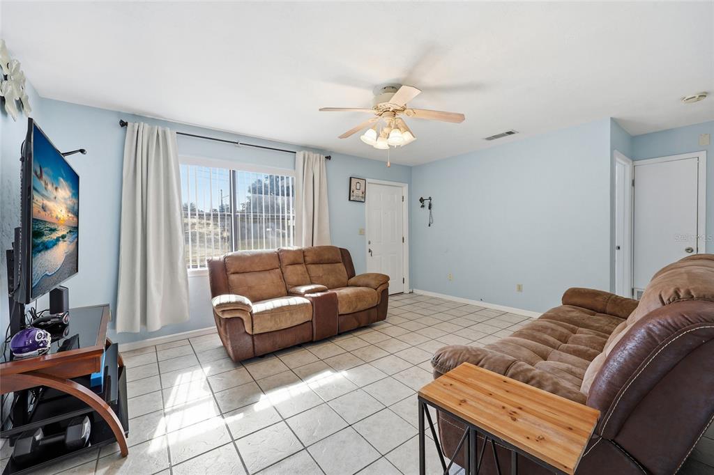 A living room with light blue walls, tile flooring, two brown sofas, and a ceiling fan — 4916 SW 57TH DRIVE, GAINESVILLE, FL