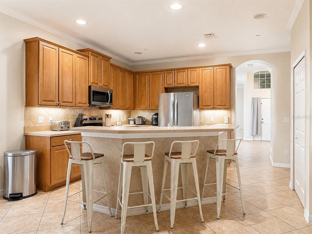 A kitchen with wood cabinets, stainless steel appliances, a tiled island, and four bar stools — 10205 CYPRESS VINE DRIVE, ORLANDO, FL