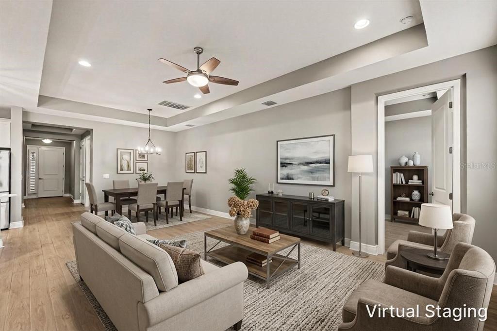 A living and dining area with a tray ceiling, wood-look flooring, and virtual furniture staging — 3714 WILD BLOSSOM PLACE, PARRISH, FL