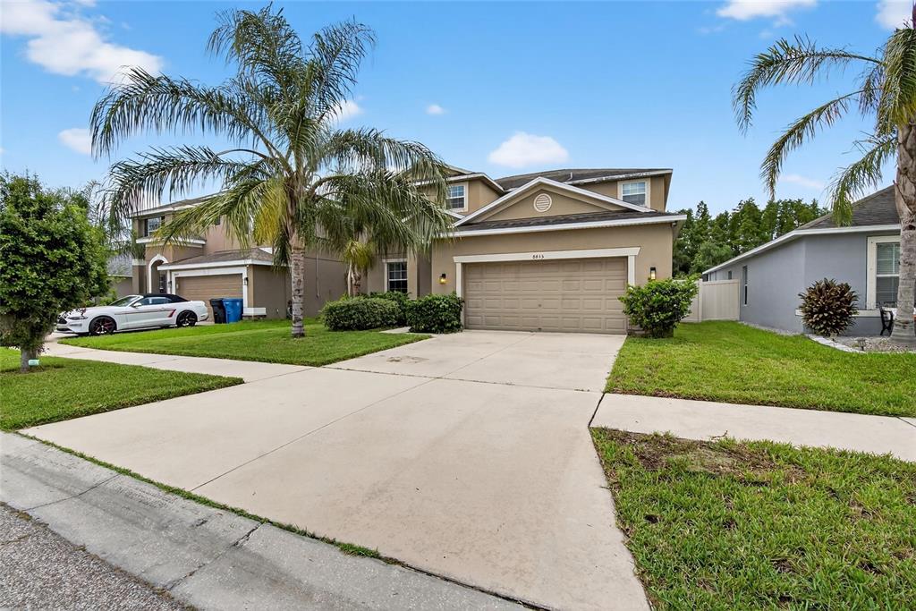 A two-story suburban house with a tan exterior, a two-car garage, and palm trees — 8435 HUNTERS FORK LOOP, RUSKIN, FL