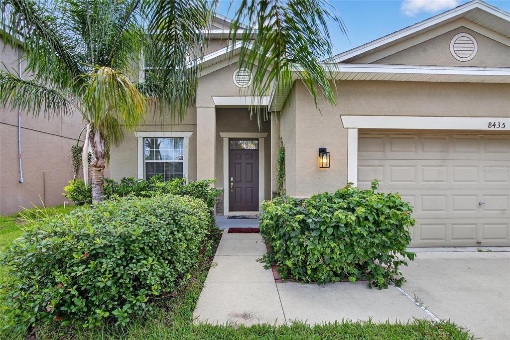 A two-story suburban house features a tan stucco exterior, a front door, and a garage — 8435 HUNTERS FORK LOOP, RUSKIN, FL