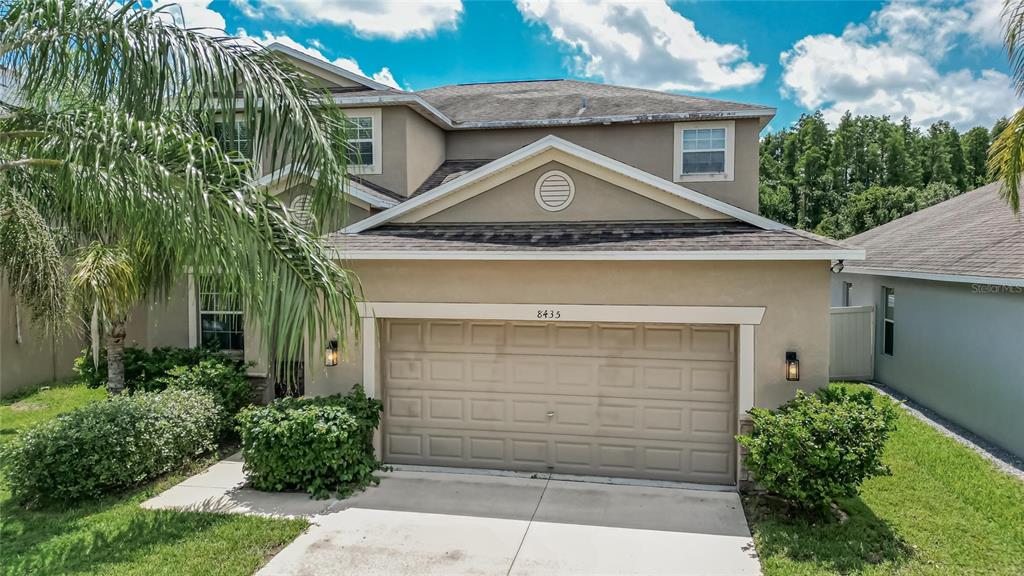 A two-story suburban house with a tan stucco exterior, a two-car garage, and landscaping — 8435 HUNTERS FORK LOOP, RUSKIN, FL