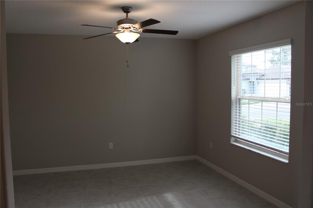 An empty room features gray tile flooring, neutral walls, a ceiling fan, and a window — 12916 WILDFLOWER MEADOW DRIVE, RIVERVIEW, FL