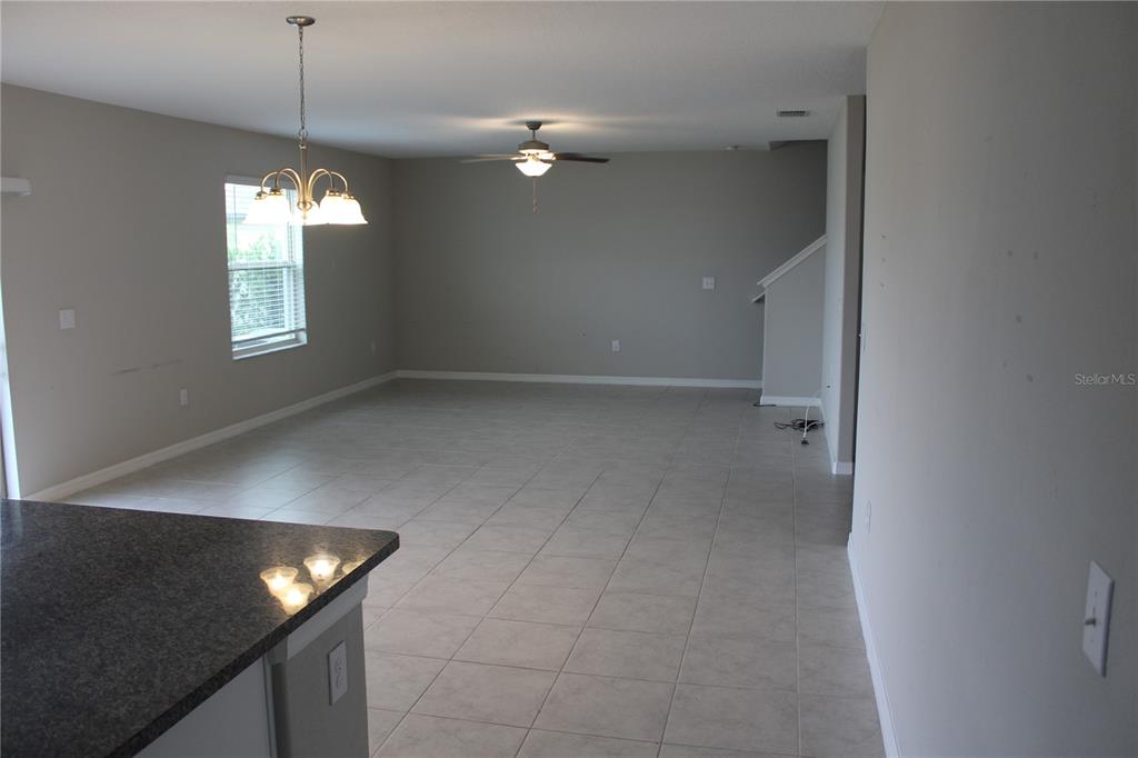 An open-concept living area features light-colored tile flooring, a ceiling fan, and a dining chandelier — 12916 WILDFLOWER MEADOW DRIVE, RIVERVIEW, FL