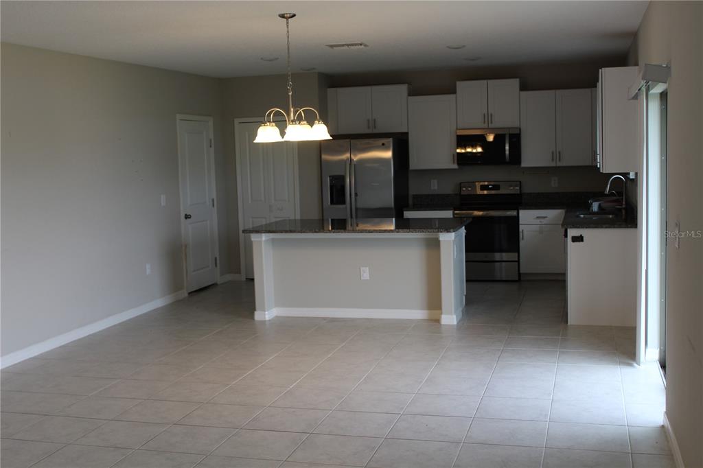 A kitchen with white cabinets, stainless steel appliances, and a granite-topped island with pendant lighting — 12916 WILDFLOWER MEADOW DRIVE, RIVERVIEW, FL