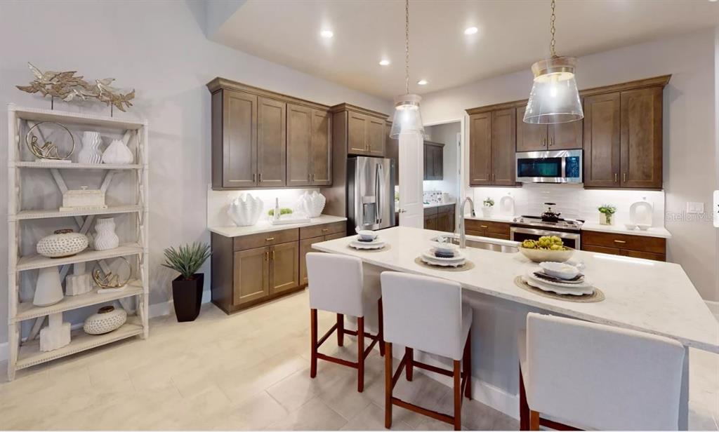 A kitchen features brown cabinets, a white quartz island with three chairs, and light flooring — 52 BRIGHTON LANE, ORMOND BEACH, FL