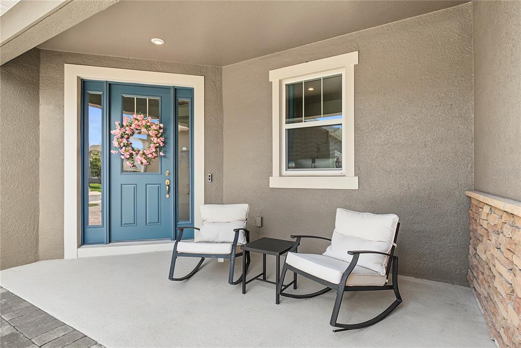 A covered front porch features a blue door, a window, and two rocking chairs — 17077 WINGSPREAD LOOP, WINTER GARDEN, FL