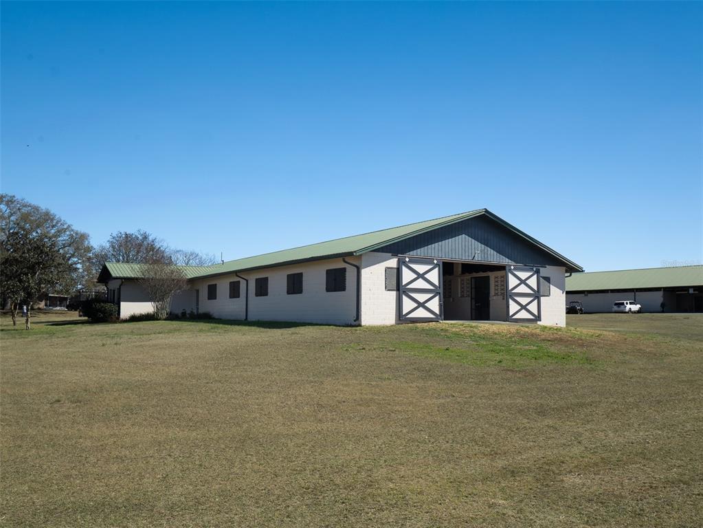 A long, single-story barn with a green metal roof sits on a grassy field — 11122 W HIGHWAY 326, OCALA, FL