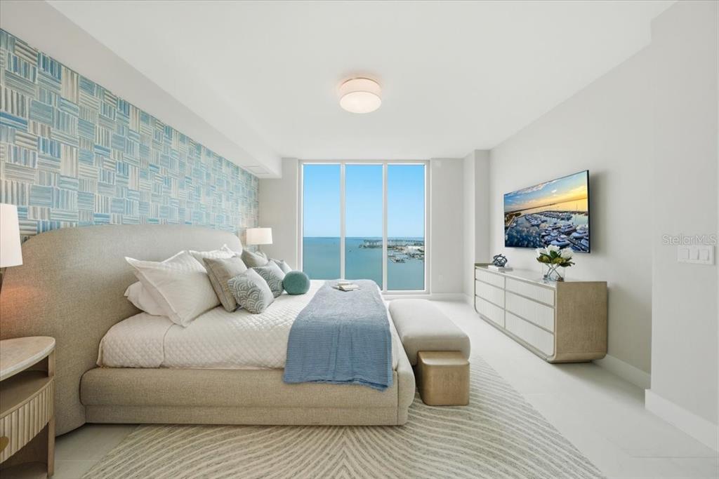 A bedroom features a patterned blue accent wall, a large bed, and floor-to-ceiling water views — 5713 BOWEN DANIEL DRIVE UNIT 1402, TAMPA, FL