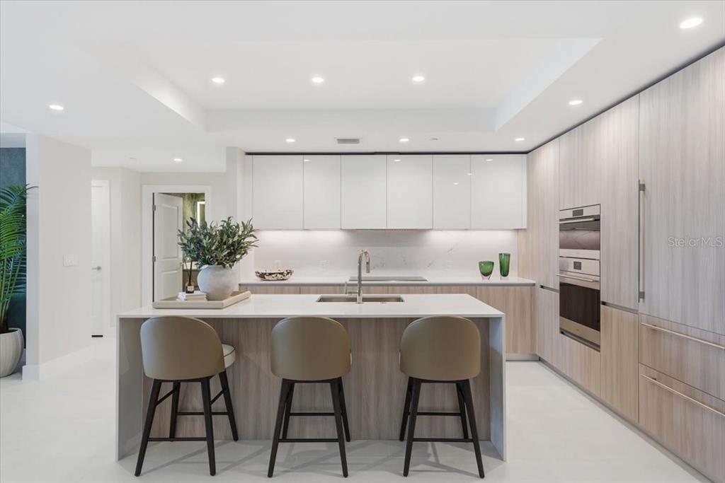 A modern kitchen features a central island with bar stools, light wood cabinetry, and white countertops — 5713 BOWEN DANIEL DRIVE UNIT 1402, TAMPA, FL