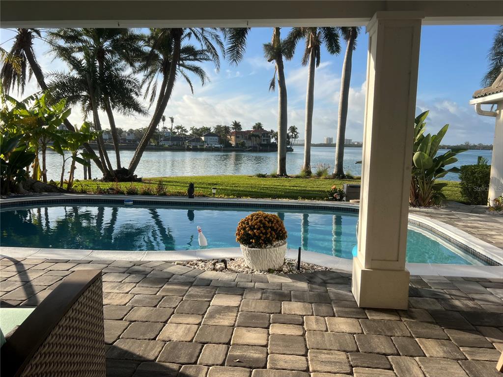 A covered patio with stone pavers overlooks a swimming pool and a waterfront view — 102 SEAGULL LANE, SARASOTA, FL