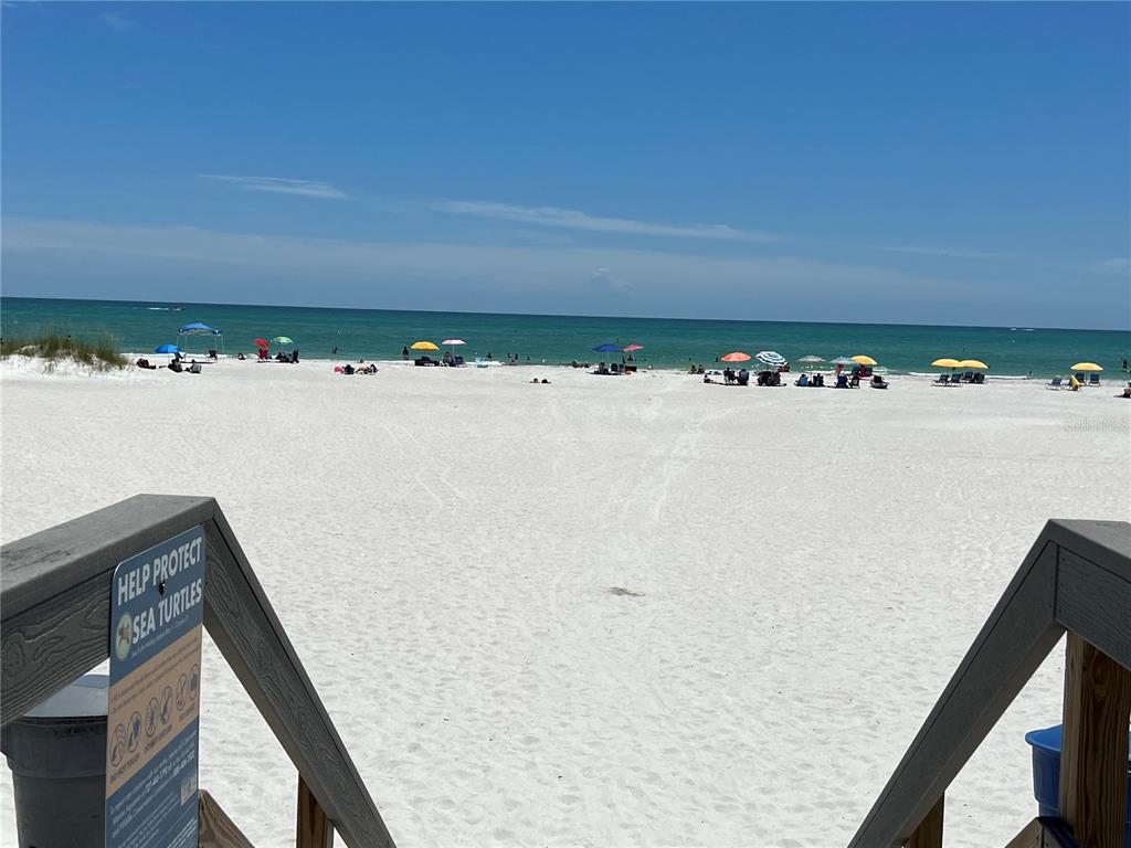 A view of a white sand beach with colorful umbrellas and the ocean beyond — 11650 CAPRI CIRCLE S UNIT 204, TREASURE ISLAND, FL