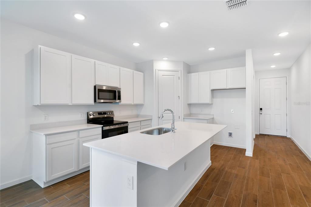 A modern kitchen features white cabinetry, quartz countertops, a center island, and wood-look tile flooring — 5315 MICKEY AVENUE, WINTER HAVEN, FL