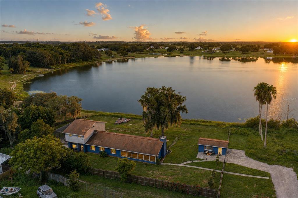 An aerial view shows a blue house with a brown roof beside a large lake — 2120 HURLEY DRIVE, BARTOW, FL